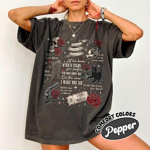 K&ouml;nnte beinhalten: Dunkelgraues T-Shirt mit einem Grafikdesign mit einem Totenkopf, Rosen, einer Katze und Text. Der Text enth&auml;lt S&auml;tze wie &bdquo;Run, Little Mouse&ldquo; und &bdquo;Let me know which stars you prefer&ldquo;. Das Shirt hat einen Vintage-Look.