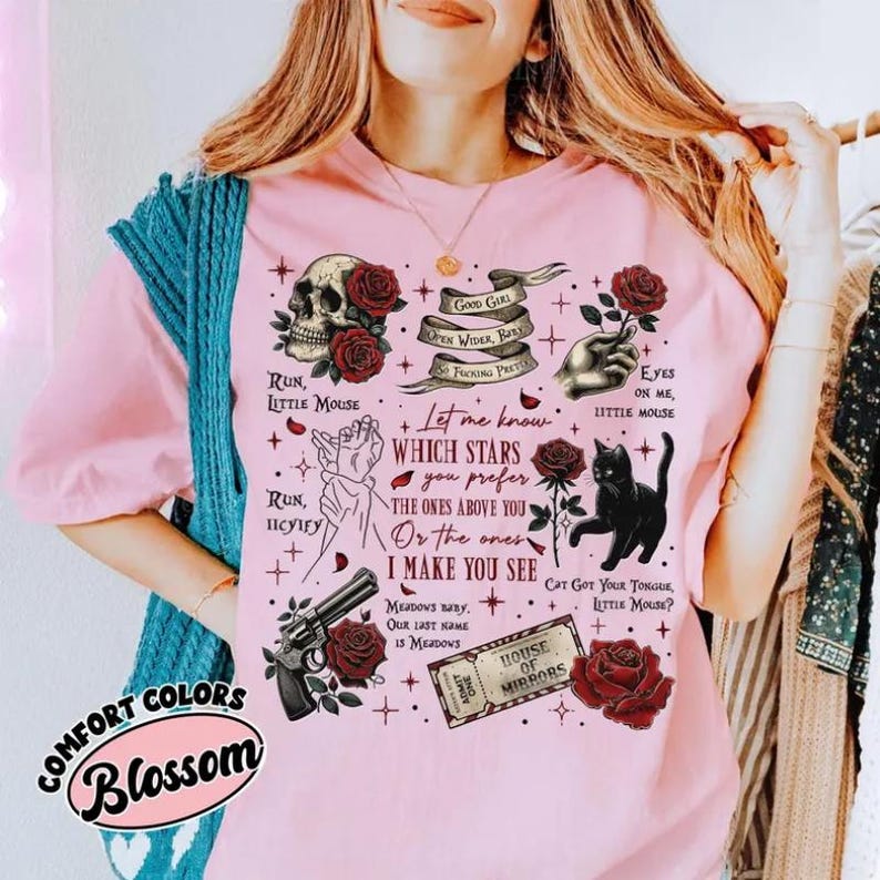 K&ouml;nnte beinhalten: Hellrosa T-Shirt mit einem Grafikdesign, das einen Totenkopf, Rosen, eine schwarze Katze, eine Pistole und verschiedene Phrasen zeigt. Das Shirt hat auch den Text "COMFORT COLORS Blossom".