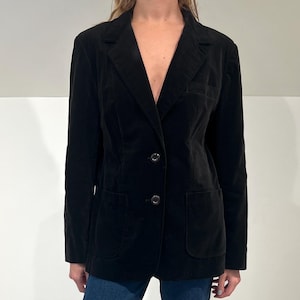 Puede incluir: Un blazer negro de terciopelo con dos botones y dos bolsillos delanteros. El blazer se combina con vaqueros azules y botines negros. El conjunto es adecuado para una variedad de ocasiones.