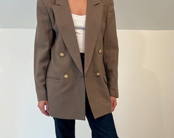 Könnte beinhalten: Ein brauner, zweireihiger Blazer mit goldenen Knöpfen. Der Blazer wird mit einem weißen Oberteil, dunkelblauen Jeans und schwarzen Stiefeln getragen. Die Jeans sind an den Knöcheln umgeschlagen.