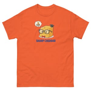 May include: Orange t-shirt featuring a cartoon cheese character wearing glasses, a bow tie, and a graduation cap. The cheese is thinking about a book and lightbulb. The text "SHARP CHEDDAR" is below the cheese.