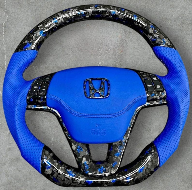 Puede incluir: Un volante de coche personalizado con un centro de cuero azul y empu&ntilde;aduras azules perforadas. El volante presenta un dise&ntilde;o de fibra de carbono con detalles azules y un emblema de Honda. El volante tiene controles integrados y el texto "SRS AIRBAG".