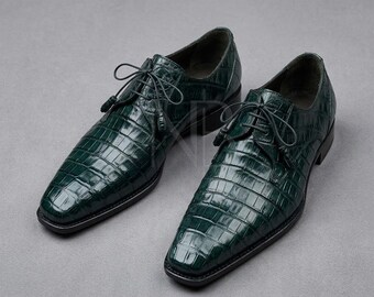 May include: A pair of dark green lace-up dress shoes featuring a glossy finish and a textured crocodile skin pattern. The shoes have a pointed toe, thin matching laces, and a low heel, showcasing a structured design with visible stitching.