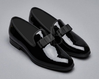 May include: A pair of black patent leather loafers featuring a high-gloss finish and a matching black grosgrain ribbon bow detail on the vamp. The slip-on shoes have a rounded toe, a low heel, and a clean, structured silhouette.