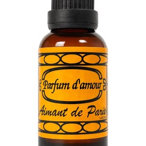 May include: A brown glass bottle with a black cap and a yellow label. The label features the text "Parfum d'amour Aimant de Paris" in black script. The bottle is likely a fragrance or essential oil.