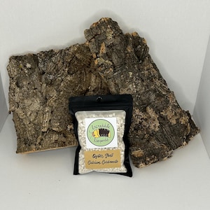 May include: A small bag of white oyster shell calcium carbonate, labeled "Incredible Isopods Oyster Shell Calcium Carbonate", next to a piece of brown bark.