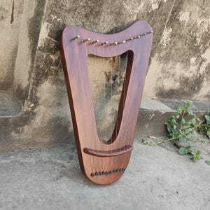 Op de afbeelding: Een houten lier met snaren, een bruine afwerking en een gebogen vorm. De lier heeft een brug en stemknoppen.