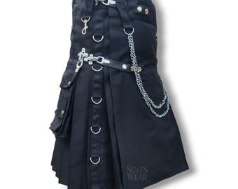 Può includere: Kilt nero con elementi metallici color argento, tra cui una catena, anelli a D e chiusure. Il kilt presenta pieghe, tasche e una cintura in pelle. Il testo "SCOTS WEAR" è visibile in basso a destra.