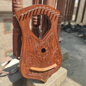 May include: A wooden lyre with a floral design carved into the body. The lyre has 10 strings and a wooden bridge.