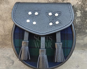 May include: A black leather sporran with a blue and green tartan pattern and three black tassels. The sporran has a flap with two Celtic knot designs and silver studs.