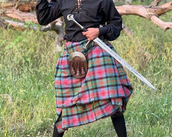 Può includere: Una persona con camicia nera, kilt e berretto, che tiene una spada. Il kilt presenta un motivo a quadri rossi, verdi, blu e neri. Un sporran in pelle marrone è appeso al kilt. La persona si trova in un'area erbosa.
