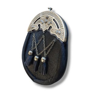 Pu&ograve; includere: Un sporran nero con un cantle argentato con disegni di cardi. Lo sporran ha tre nappe nere appese a catene d'argento. La borsa &egrave; realizzata in un materiale scuro e strutturato.