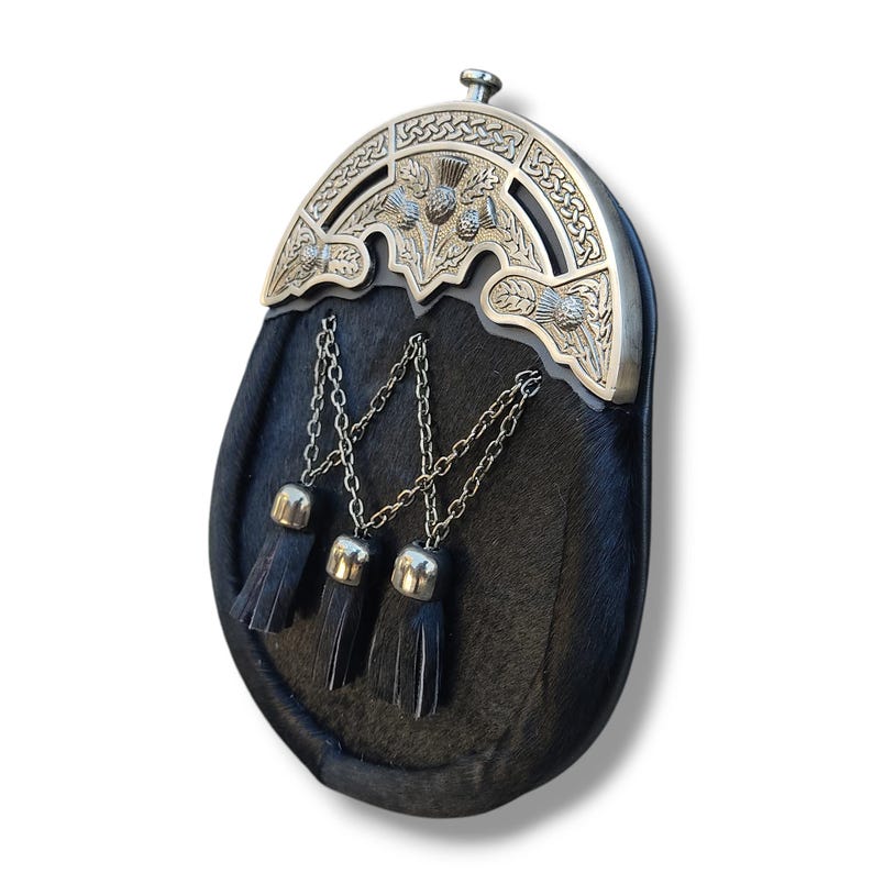 Pu&ograve; includere: Un sporran nero con un cantle argentato con disegni di cardi. Lo sporran ha tre nappe nere appese a catene d'argento. La borsa &egrave; realizzata in un materiale scuro e strutturato.