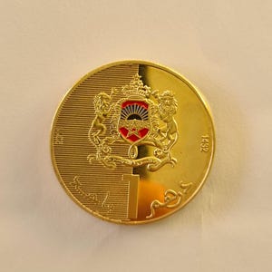 Könnte beinhalten: Eine goldene Münze mit einem detaillierten Emblem, das zwei Löwen, eine Krone und einen Stern zeigt, sowie die Zahl "1" und das Jahr "1452". Die Münze hat eine glänzende, reflektierende Oberfläche.
