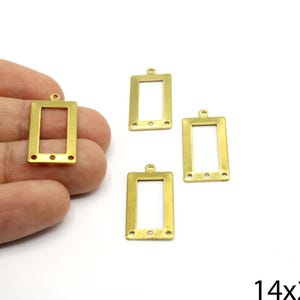 May include: Four gold-toned metal rectangular frame charms with a hole at the top for hanging. Each frame has a small hole on each side. The frames measure 14x23mm.