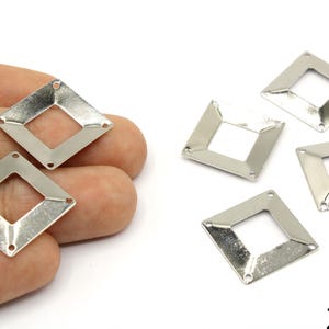 Könnte beinhalten: Silberfarbene Metallverbinder in Diamantenform mit quadratischem Ausschnitt in der Mitte. Jeder Verbinder hat drei kleine Löcher an den Ecken. Die Verbinder sind ca. 2 cm groß.