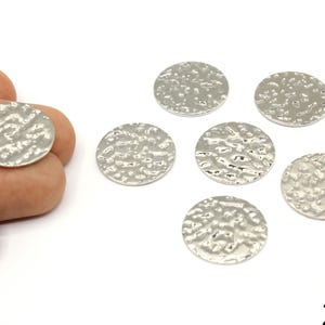 May include: Silver-colored, hammered-texture metal disc charms. One charm is held by a hand, with five more scattered nearby. Each disc is approximately 20mm in diameter, suitable for jewelry making or crafting projects.