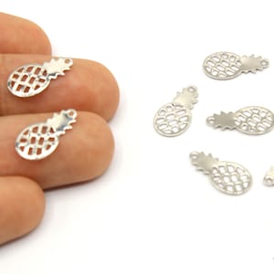 May include: Silver-colored pineapple charms, approximately 0.5 inches in length, are displayed against a white background. The charms have a cut-out design, and some are held by a hand. The image also includes the measurement "12mm".