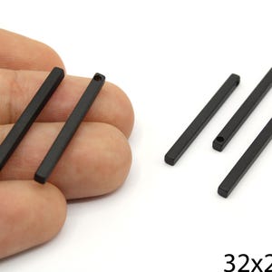 May include: Several matte black rectangular metal bars with a hole at one end. The bars are 3.2cm long and 0.25cm wide. Some bars are held in a hand, while others are on a white surface.