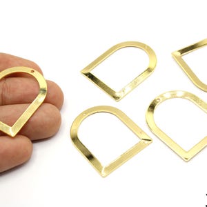 Puede incluir: Hallazgos de joyería de metal dorado en forma de arco. Los hallazgos tienen la parte posterior abierta con un pequeño agujero en la parte superior para sujetarlos. La imagen muestra cuatro hallazgos, uno de ellos en la mano. El tamaño es de 35 mm.