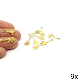 May include: Gold-colored star charms with a small loop at the top and a thin bar. The charms are approximately 0.75 inches long and 0.35 inches wide. Several charms are scattered on a white surface.