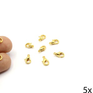 May include: A collection of small, gold-colored lobster claw clasps. These jewelry findings are scattered on a white surface. The clasps are approximately 5mm x 10mm in size.