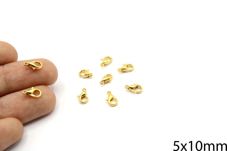 May include: A collection of small, gold-colored lobster claw clasps. These jewelry findings are scattered on a white surface. The clasps are approximately 5mm x 10mm in size.