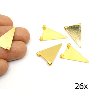 May include: Gold-coloured triangle charms with small loops at the corners. The charms are arranged on a white surface, with one held in a hand. The image includes the text "26x17mm".