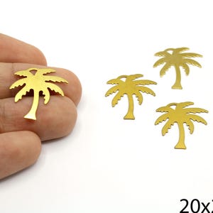 May include: Four gold palm tree charms, each measuring 20mm by 24mm. The charms are shown on a hand, with one charm held between two fingers.