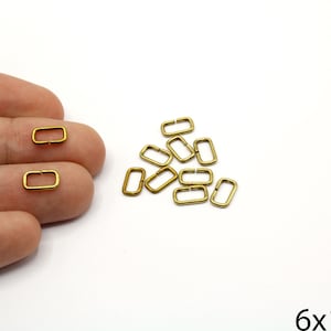 May include: A group of 10 gold-toned metal rectangular rings, each measuring 6 by 10 millimetres. The rings are arranged in a pile on a white surface.
