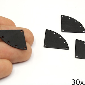 May include: Black metal half-circle findings with multiple holes for crafting. The findings are approximately 1.18 x 0.79 inches. The image shows several pieces, with one held in a hand.