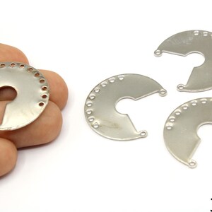 Puede incluir: Hallazgos de joyería en forma de media luna de metal plateado. Cada pieza tiene una serie de pequeños agujeros a lo largo del borde curvo y dos agujeros en las puntas. La imagen muestra varias piezas, una de ellas en una mano. El texto "30mm" es visible.