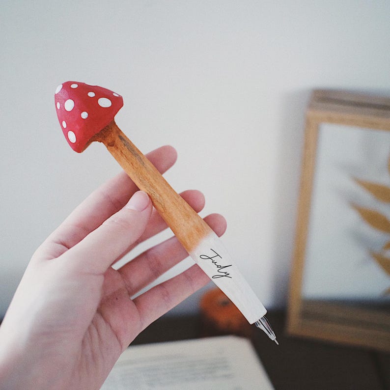 K&ouml;nnte beinhalten: Ein skurriler Stift in Pilzform mit roter Kappe und wei&szlig;en Punkten. Der Holzschaft geht in einen wei&szlig;en Bereich &uuml;ber, auf dem der Name "Judy" steht. Dieser Stift ist ein einzigartiges Schreibger&auml;t, ideal f&uuml;r Schreibwarenliebhaber.