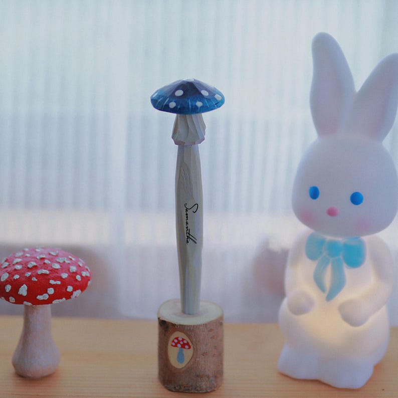 K&ouml;nnte beinhalten: Eine skurrile Sammlung dekorativer Gegenst&auml;nde. Ein roter Pilz mit wei&szlig;en Punkten, ein pilzf&ouml;rmiger Stift mit dem Namen "Samantha" und ein wei&szlig;es Hasen-Nachtlicht mit einer blauen Schleife.