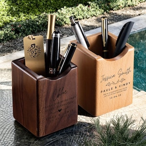May include: Two wooden pen holders, one dark brown and one light brown, each holding pens and a decorative tag. The dark brown holder has the name "Chloe" and text. The light brown holder has the name "Jessica Smith" and text. Pens are black, silver, and gold.