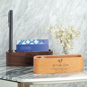 Peut inclure: Deux organiseurs de bureau en bois. L'un est brun foncé avec un stylo et une carte bleue et blanche. L'autre est brun clair avec le texte "Mr. & Mrs. Small THANKS FOR BEING PART OF OUR CELEBRATION! 20TH JANUARY 2024".