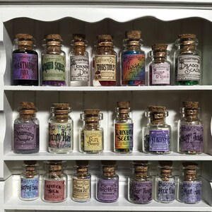 May include: A white shelf unit holds numerous small glass bottles with corks. Each bottle is labelled with names such as "Nightmare Fuel" and "Dragon Scale." The bottles contain colourful substances, creating a whimsical apothecary display.