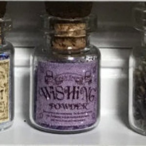 Könnte beinhalten: Drei kleine Glasflaschen mit Korken. Die mittlere Flasche hat ein lila Etikett mit der Aufschrift "Wishing Powder" in einer dekorativen Schriftart. Die Flasche enthält lila Glitzer. Andere Flaschen haben Etiketten mit Text.