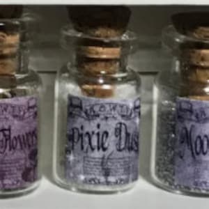 May include: Three small glass bottles with cork stoppers and purple labels. The labels read "Fairy Flowers", "Pixie Dust", and "Moon". The bottles are filled with different colored contents.