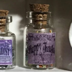Könnte beinhalten: Kleine, klare Glasflaschen mit Korken. Eine Flasche hat ein lila Etikett mit der Aufschrift "Happy Thoughts" in verschnörkelter Schrift. Die Flasche enthält bunte Objekte. Die andere Flasche hat ein lila Etikett mit der Aufschrift "Stardust".