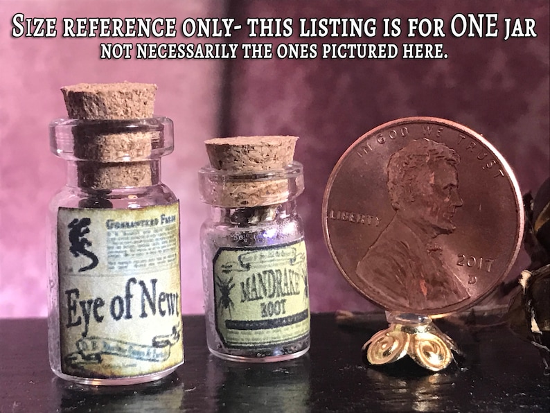 May include: Two small glass jars with cork stoppers, labeled "Eye of Newt" and "Mandrake Root." A penny is included for size reference. The jars have vintage-style labels with illustrations. The text "SIZE REFERENCE ONLY" is at the top.