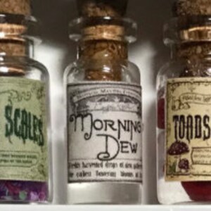 Könnte beinhalten: Drei kleine, klare Glasflaschen mit Korken und Etiketten. Die Etiketten lauten "Dead Scales", "Morning Dew" und "Toadstools". Die Flaschen enthalten farbige Inhalte, darunter lila, klare und rote Substanzen.