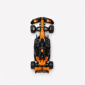 May include: Overhead shot of a black and orange race car model. The model has intricate details, including wheels, a rear wing, and sponsor logos. The car is set against a white backdrop.