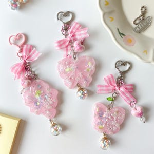 Llavero con dije de resina rosa: trébol, mariposa y cinta