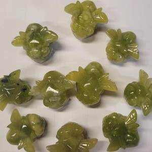 Peut inclure: Dix petites sculptures de jade vert représentant une abeille stylisée avec des ailes. Chaque sculpture est unique et présente une forme et des détails légèrement différents.