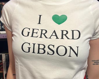 Może przedstawiać: Biała koszulka z zielonym sercem i nadrukiem "I love Gerard Gibson" z przodu.