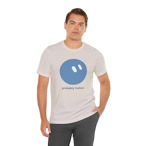 May include: A heather gray short-sleeve t-shirt featuring a large blue circle graphic with two white diagonal dashes inside. Below the circle, the text reads "probably human." in a simple black sans-serif font on the chest area.