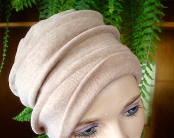 May include: A beige knit hat with a folded design. The hat is worn by a person with a dark blue scarf with floral print.