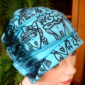 May include: A blue and black patterned hat with a black lace trim. The hat is worn by a person with a necklace.