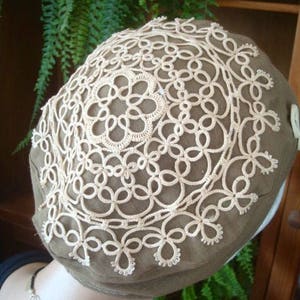 May include: A brown fabric hat with a white crocheted lace design. The lace is a delicate pattern of circles and loops.